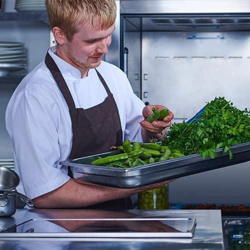 A chef inspecting vegetable ingredients that he has just taken out of the kitchen refrigerator.