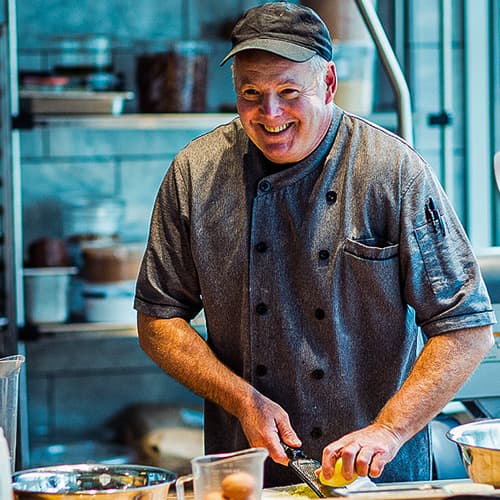 An older gentleman who is smiling, grating the zest of a lemon.